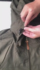 Olive green windbreaker laid flat: the hood and collar, the zip pulls, the chest and hand pockets, the cuff, and water beading off the fabric.