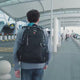 Man wearing the black anti-theft backpack through an airport, water beading on the fabric, then the zip pulls brought together, the laptop compartment opened and the inside pockets filled.
