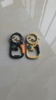 Black carabiner compass watch held in the hand: the watch face, the small compass and the carabiner clip, with a tan one beside it.