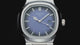 The NIBOSI 2632 with a blue dial and silver steel band turning against black, its hands glowing green in the dark, a close-up of the dial and date window, then the watch on a wrist at a keyboard.