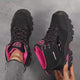 A pair of women's ankle hiking boots held up to the camera, black with rose-red trim, then the same boot in grey with rose red, showing the lug soles and padded collars.