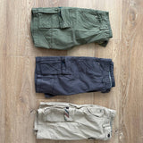Customer photo of three pairs as delivered: Army Green, Dark Grey and Khaki six-pocket cargo shorts folded flat on a timber floor