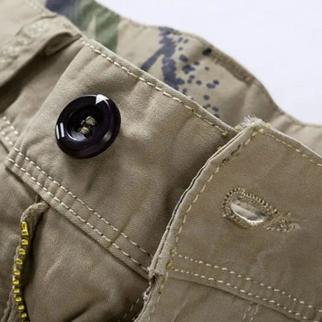 Close-up of the dark four-hole waistband button and stitched buttonhole on the khaki RELAX shorts, camouflage print showing on the inner waistband
