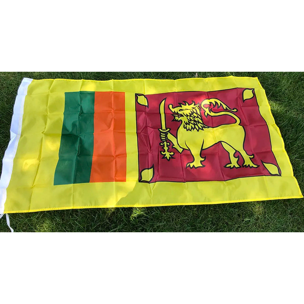 Sri Lankan flag in printed polyester laid flat on grass: gold lion with sword on maroon, green and orange bands, yellow edge