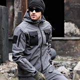 Man kneeling in the grey softshell jacket with black chest pockets; beanie, sunglasses, gloves, trousers not included