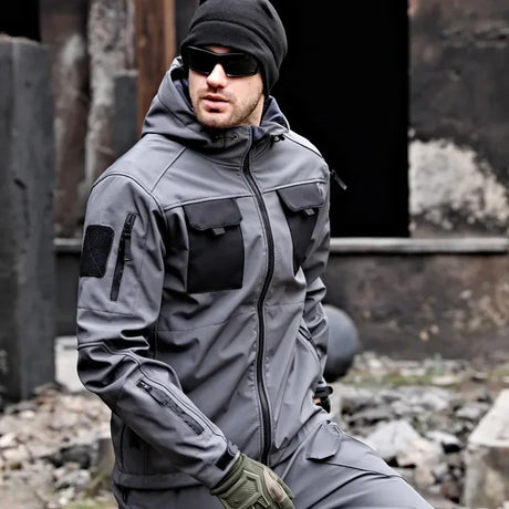 Man kneeling in the grey softshell jacket with black chest pockets; beanie, sunglasses, gloves, trousers not included