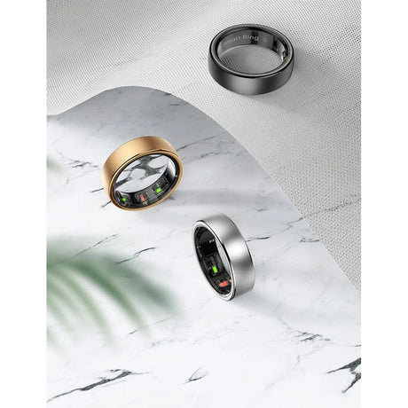 Black, gold and silver R10 smart rings laid on white marble and mesh fabric