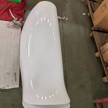 A single white tulip blade shell lying on the workshop floor beside pallets and cartons, showing its curved petal profile end on.