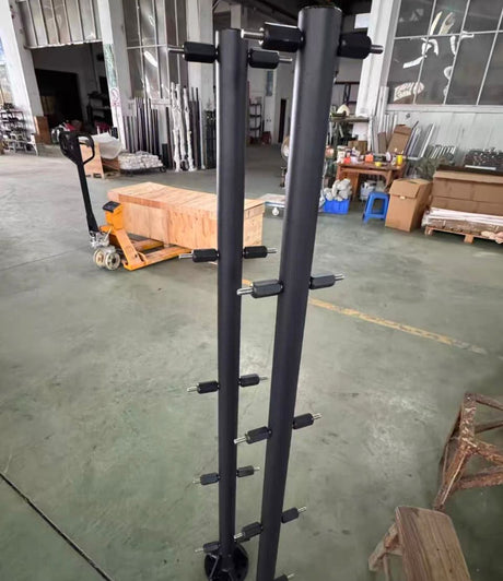 Two black steel blade-support columns standing in the workshop, each carrying five sleeved cross-pins that the blade shells bolt on to.