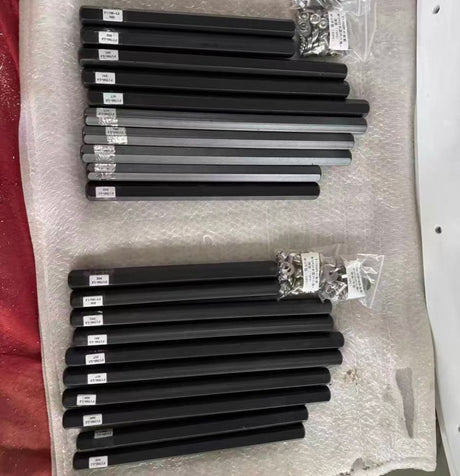 Two sets of black support bars laid out on bubble wrap, each bar carrying a printed part label, with bagged nuts and washers alongside.
