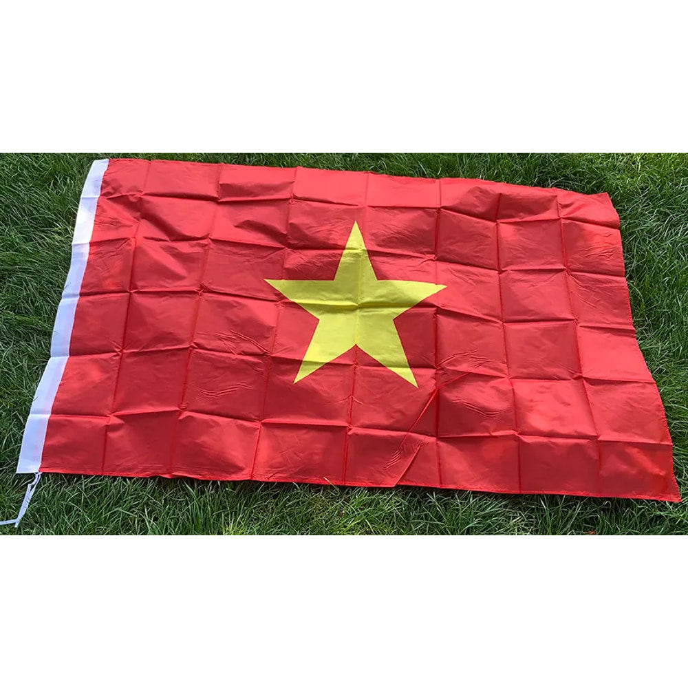 Vietnamese flag in printed polyester laid flat on grass: yellow star on red, white header strip at left