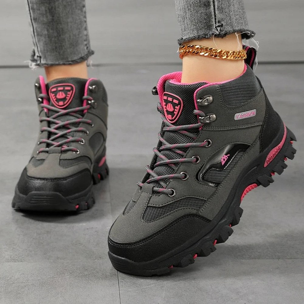 Women's ankle hiking boots in grey with rose red trim, laced up and worn, side view of the rubber lug sole