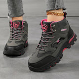 Women's ankle hiking boots in grey with rose red trim, laced up and worn, side view of the rubber lug sole