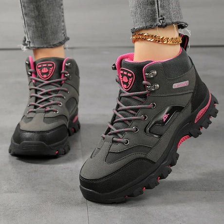 Women's ankle hiking boots in grey with rose red trim, laced up and worn, side view of the rubber lug sole