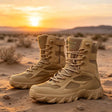 Pair of sand-coloured high lace-up field boots with mesh panels and a chunky lug sole, standing on desert sand at sunset