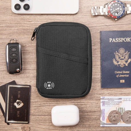Black zip pouch on a desk beside a passport, car key, bank cards and earbuds