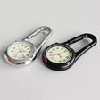 Silver and black carabiner clip watches side by side on a grey surface, luminous dials facing up