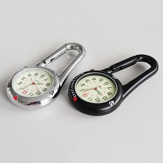 Silver and black carabiner clip watches side by side on a grey surface, luminous dials facing up