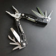 Black-coated multi-tool pliers laid open, knife, saw and screwdrivers fanned out