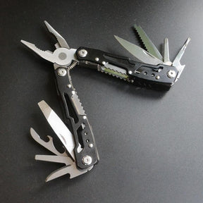 Black-coated multi-tool pliers laid open, knife, saw and screwdrivers fanned out